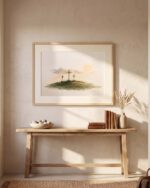 Three Crosses at Calvary print in a light oak frame with a wide mat, hanging above an oak entryway console with books, a stone bowl and dried grasses
