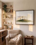 Three Crosses at Calvary canvas in a bronze frame above a linen reading chair beside built-in bookshelves in a sunlit reading corner, Luke 23:33
